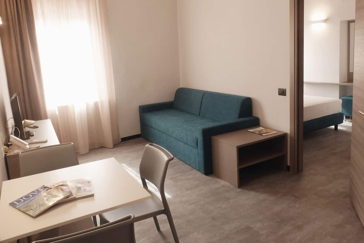 Une chambre d’hôtel de taille réduite, comprenant un lit simple, un petit bureau avec une chaise, un canapé et une table de chevet.