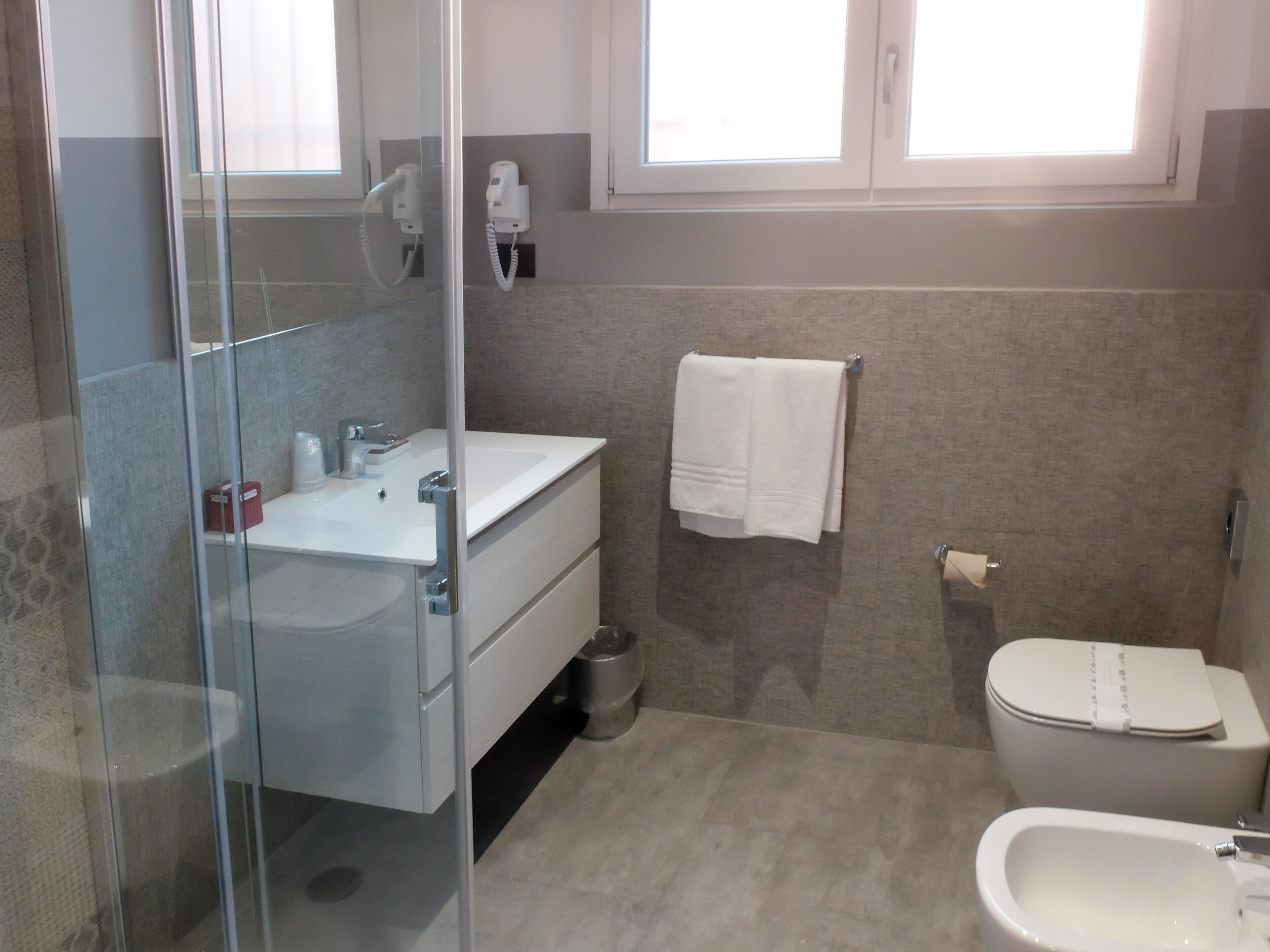 A bathroom with a glass shower enclosure, a white sink, a toilet, and a bidet.