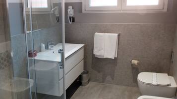 A bathroom with a glass shower enclosure, a white sink, a toilet, and a bidet.