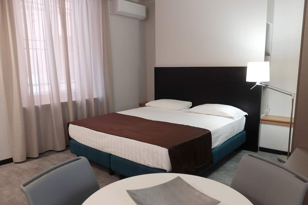Une chambre d’hôtel avec un lit, une table de chevet, une lampe, une chaise et une table ronde.