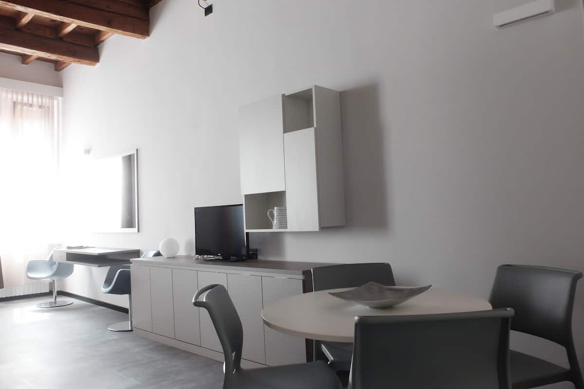 Un espace repas moderne avec une table ronde et quatre chaises, un téléviseur à écran plat posé sur un meuble, et une grande fenêtre laissant entrer la lumière naturelle.