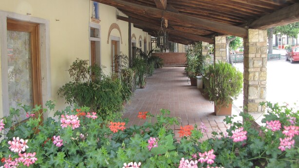 A covered walkway with potted plants and flowers, leading to a building with arched doorways and a brick wall. - Residence Casprini da Omero (Greve in Chianti)