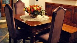 Un comedor con mesa de madera, cuatro sillas, camino de mesa de encaje y un jarrón de flores.