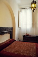 Una camera da letto con una coperta a motivi decorativi, una testiera in legno, un comodino e una lampada a sospensione.