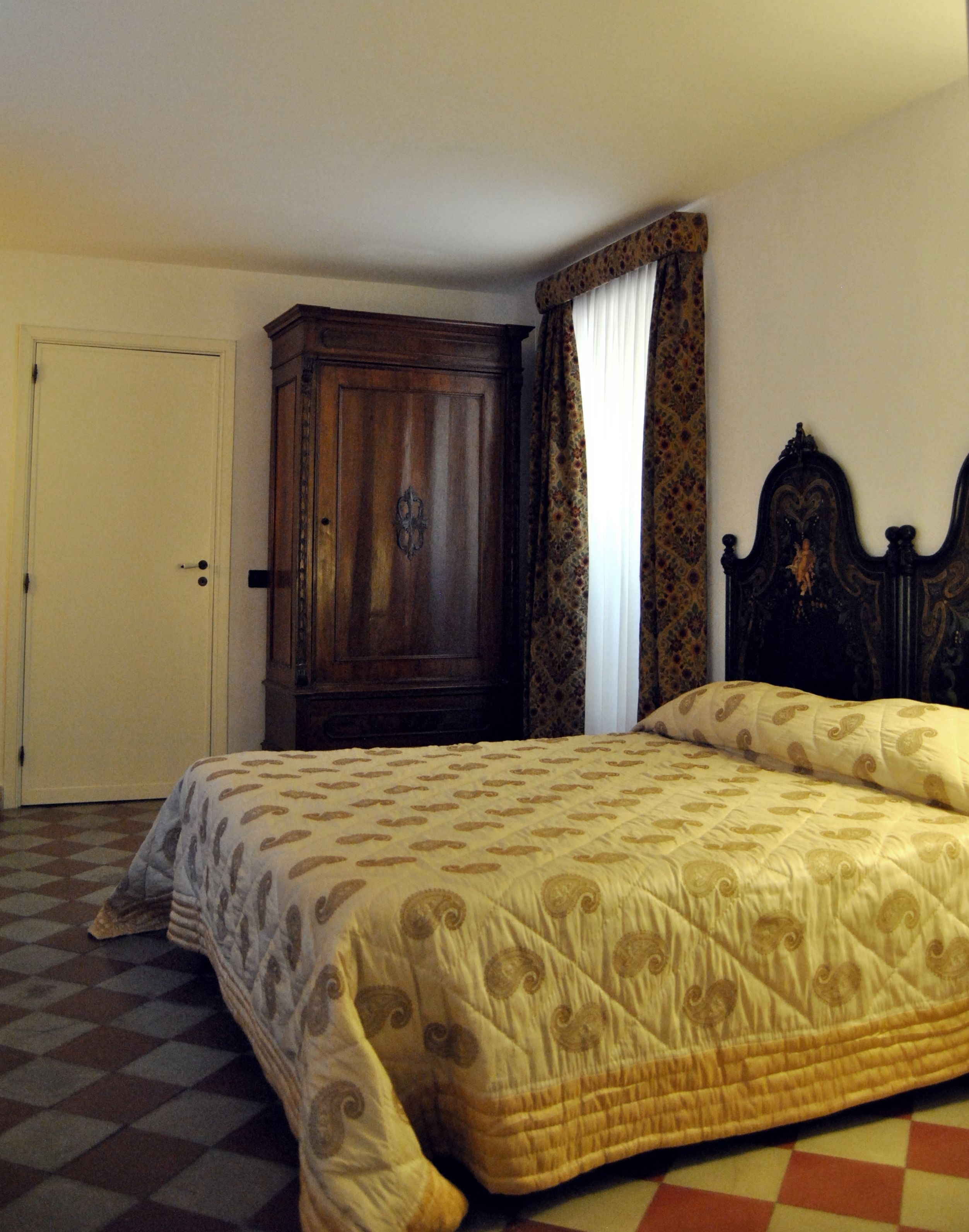 Een slaapkamer met een bed, een kledingkast, een deur en gordijnen met een patroon.