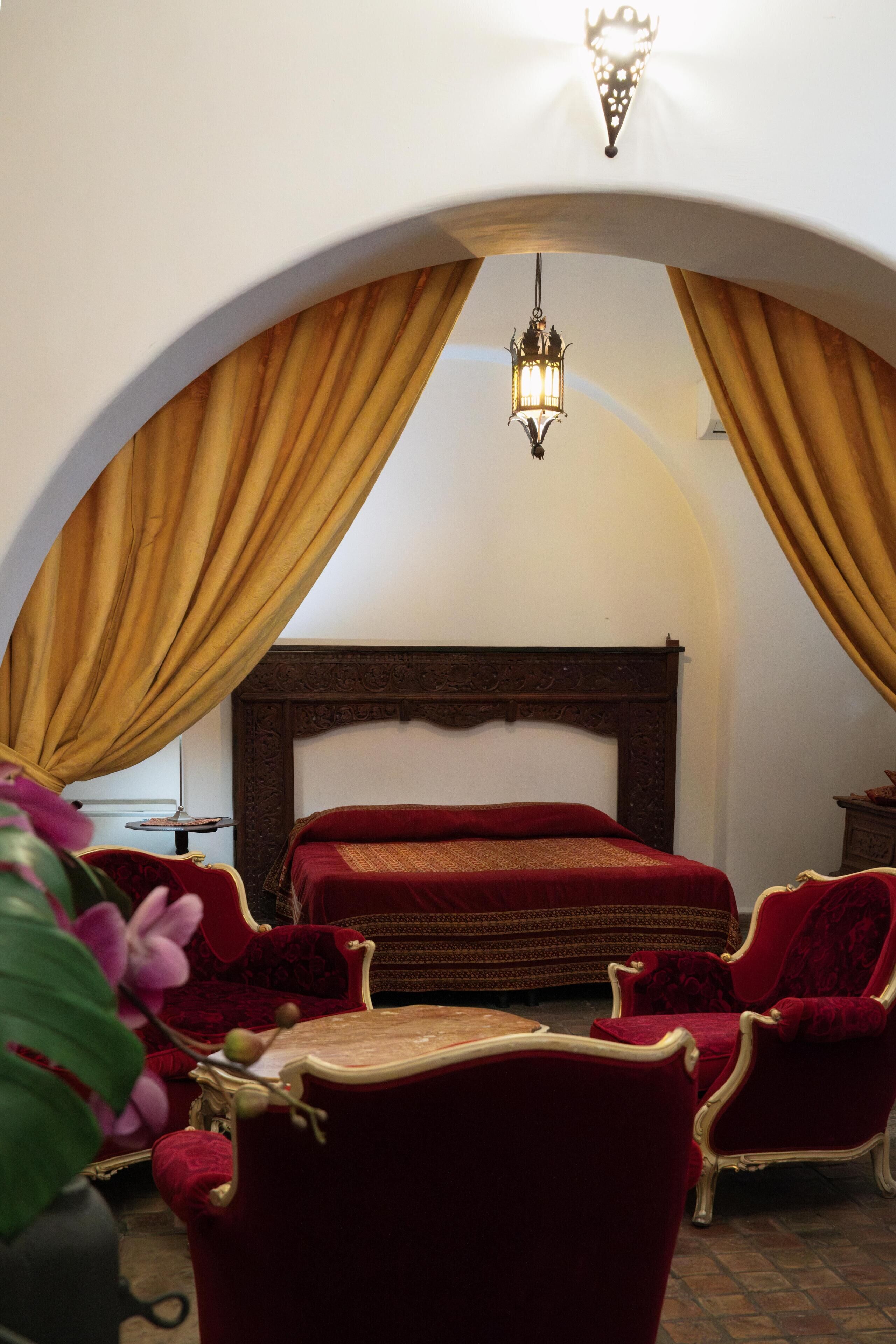 Une chambre à coucher avec un grand lit, un lustre et des meubles recouverts d’un tissu rouge.