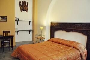 A bedroom with a bed, a chair, a desk, a lamp, and a shelf with books.