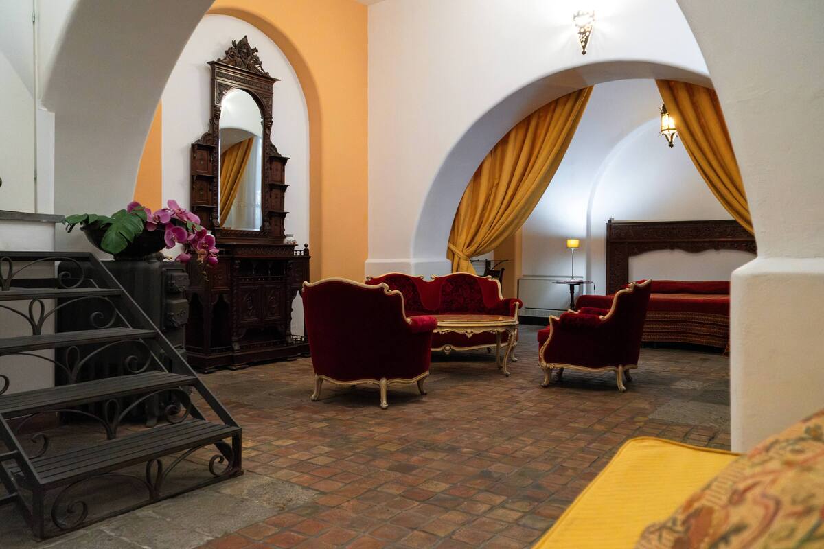 A room with a checkered floor, red velvet sofas, a wooden cabinet, and a mirror.