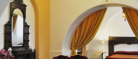 A room with an arched ceiling, a bed, two armchairs, a small table, and a mirror.