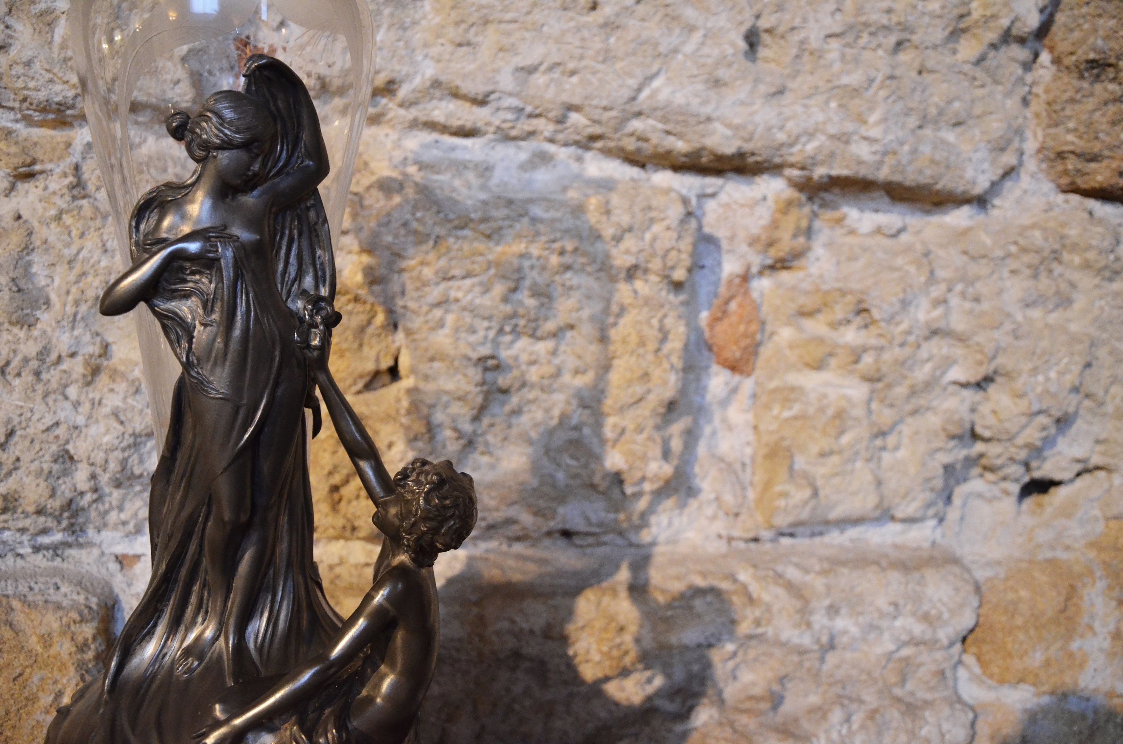 A statue of a woman holding a child against a stone wall background.