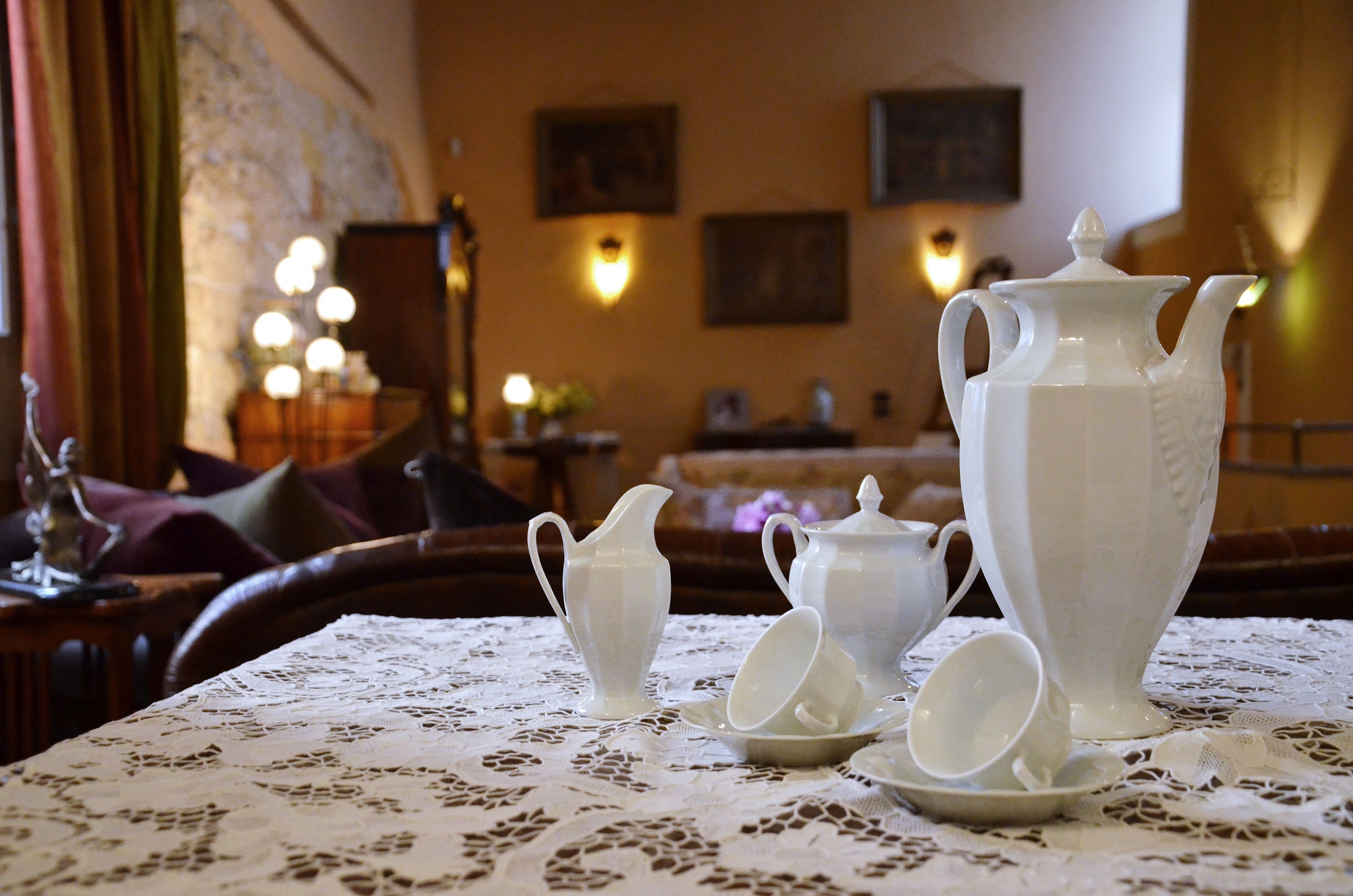 A dining table with a lace tablecloth, a pitcher, teapot, and cups.