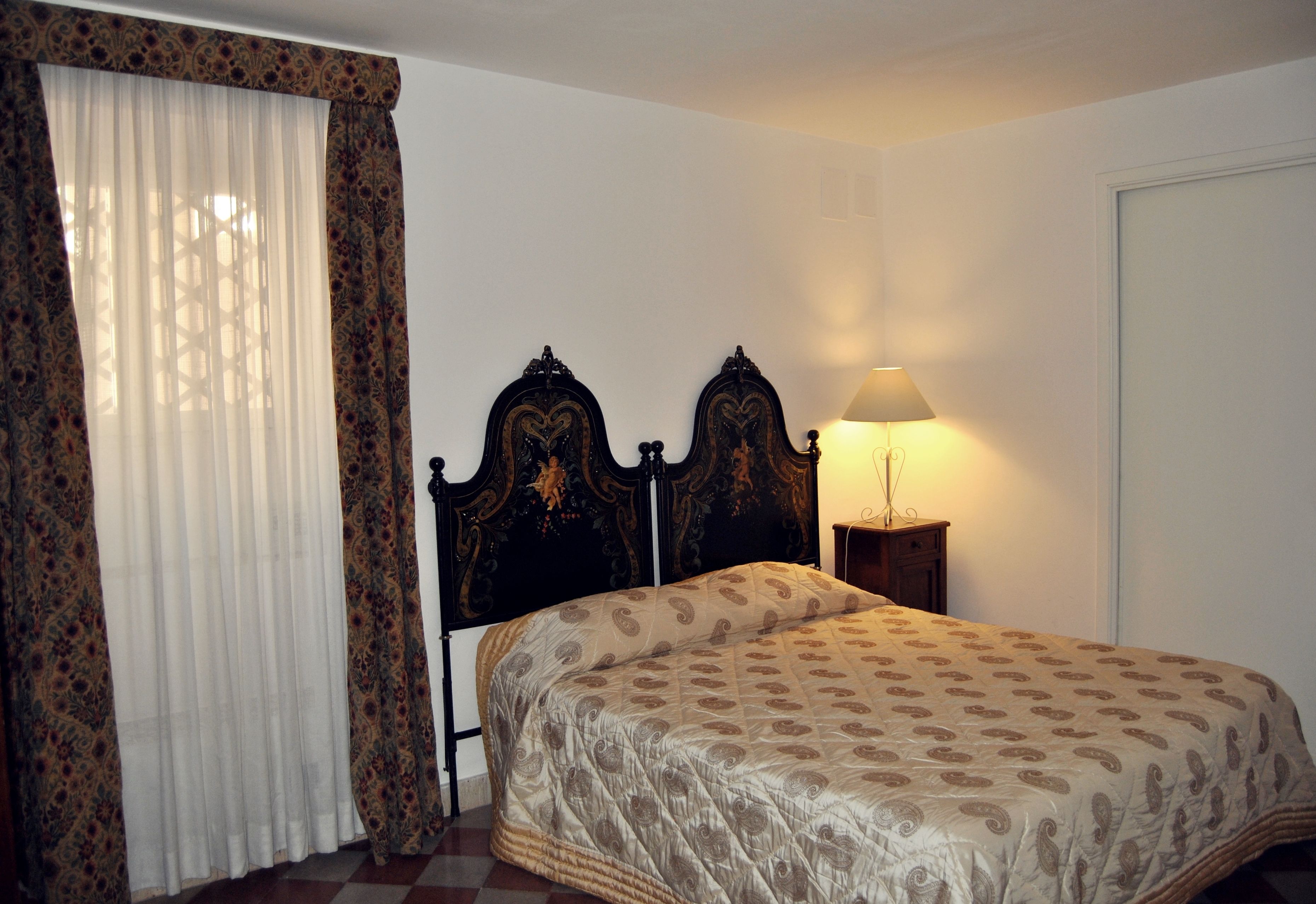 A bedroom with a bed, a nightstand, a lamp, and a window with curtains.
