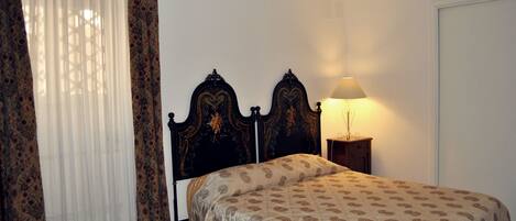 A bedroom with a bed, a nightstand, a lamp, and a window with curtains.
