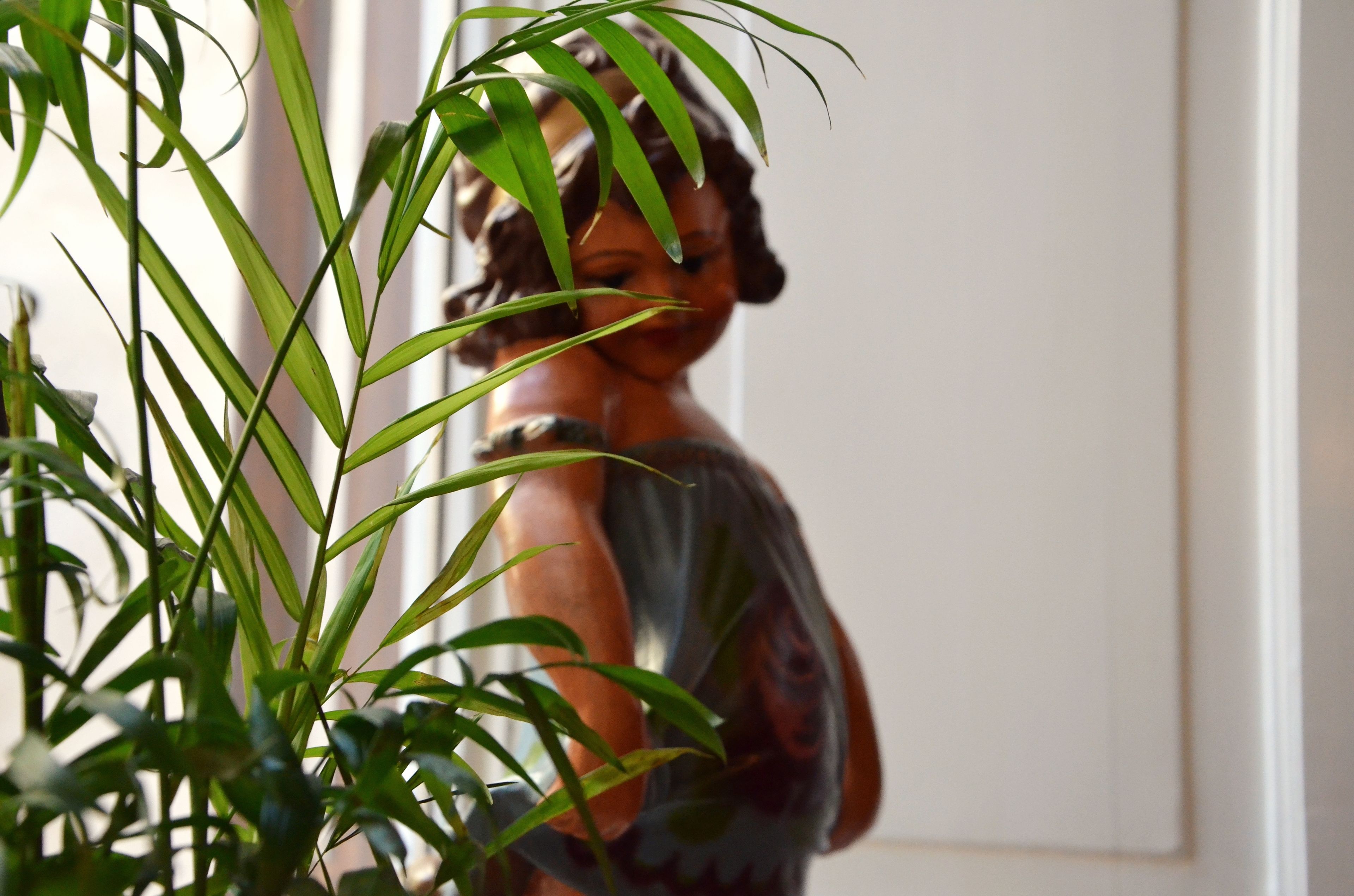 Una estatua de mujer en una habitación con una puerta blanca y una planta al frente.