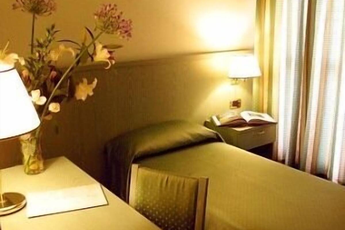 A hotel room with a single bed, a bedside table with a lamp, and a window with curtains.
