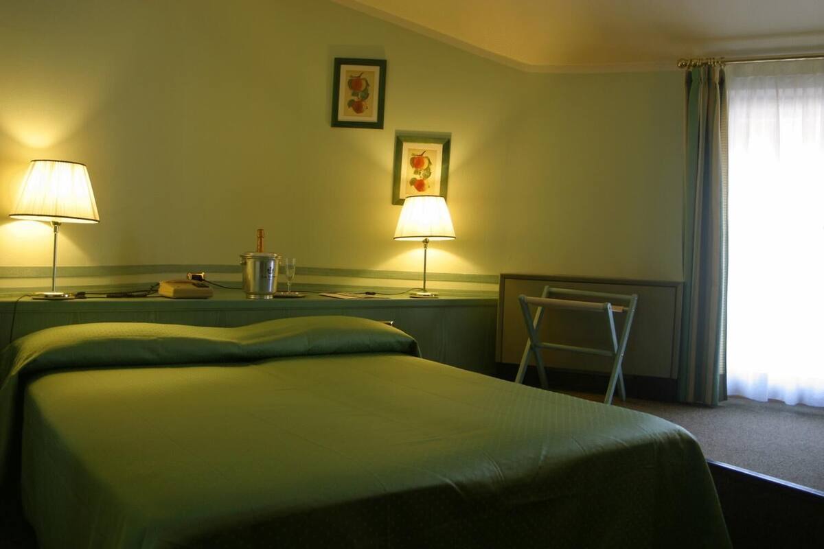 A hotel room with two beds, two lamps, a small table with a bottle and glasses, and a chair.