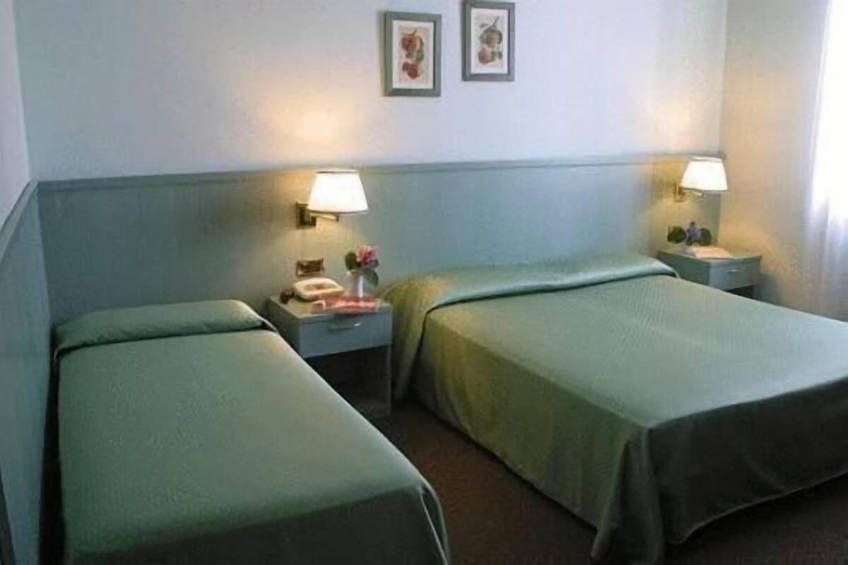 A hotel room with two single beds, a nightstand with a lamp, and a small table with a vase of flowers.