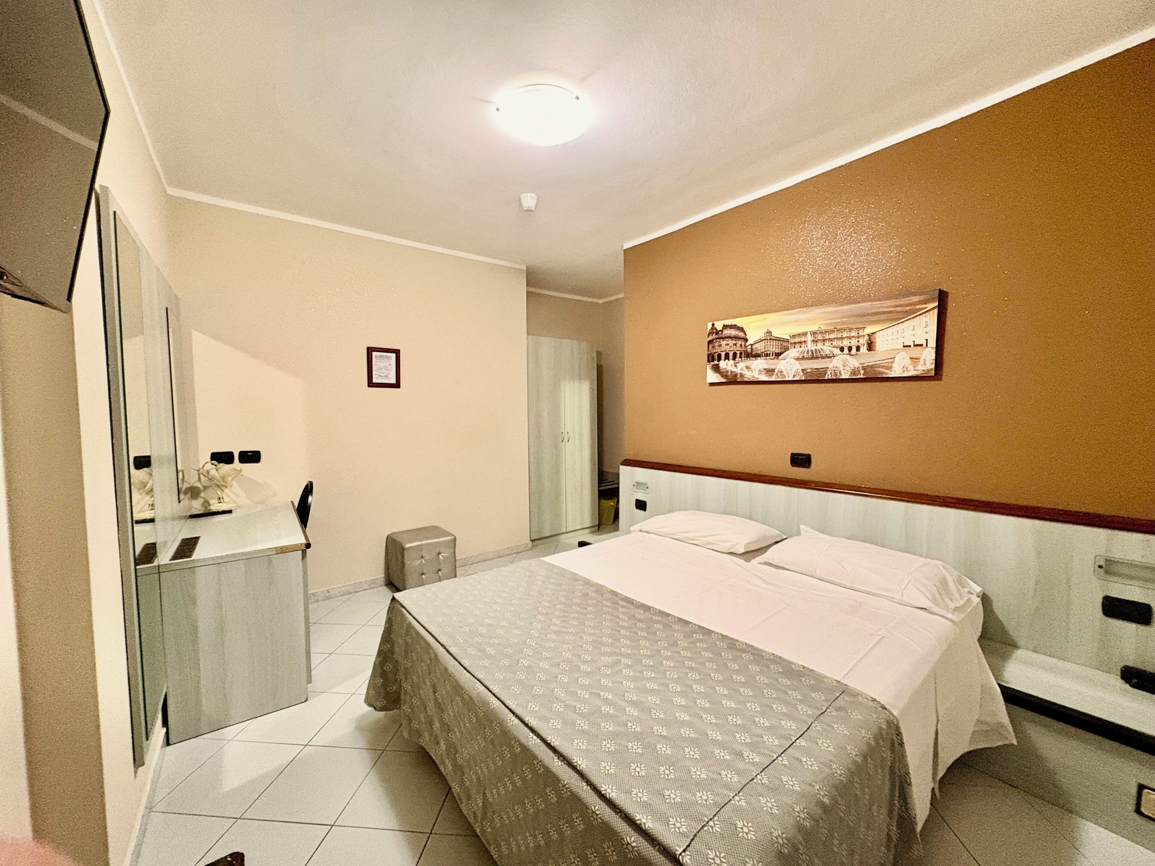 A hotel room with a bed, a dresser, a mirror, and a wall-mounted picture.