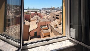 A window with a view of a cityscape, including buildings and a distant ship. - Albergo della Posta (Genoa)