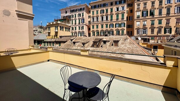 A balcony with a table and chairs, overlooking a row of historic buildings with multiple stories and balconies. - Albergo della Posta (Genoa)