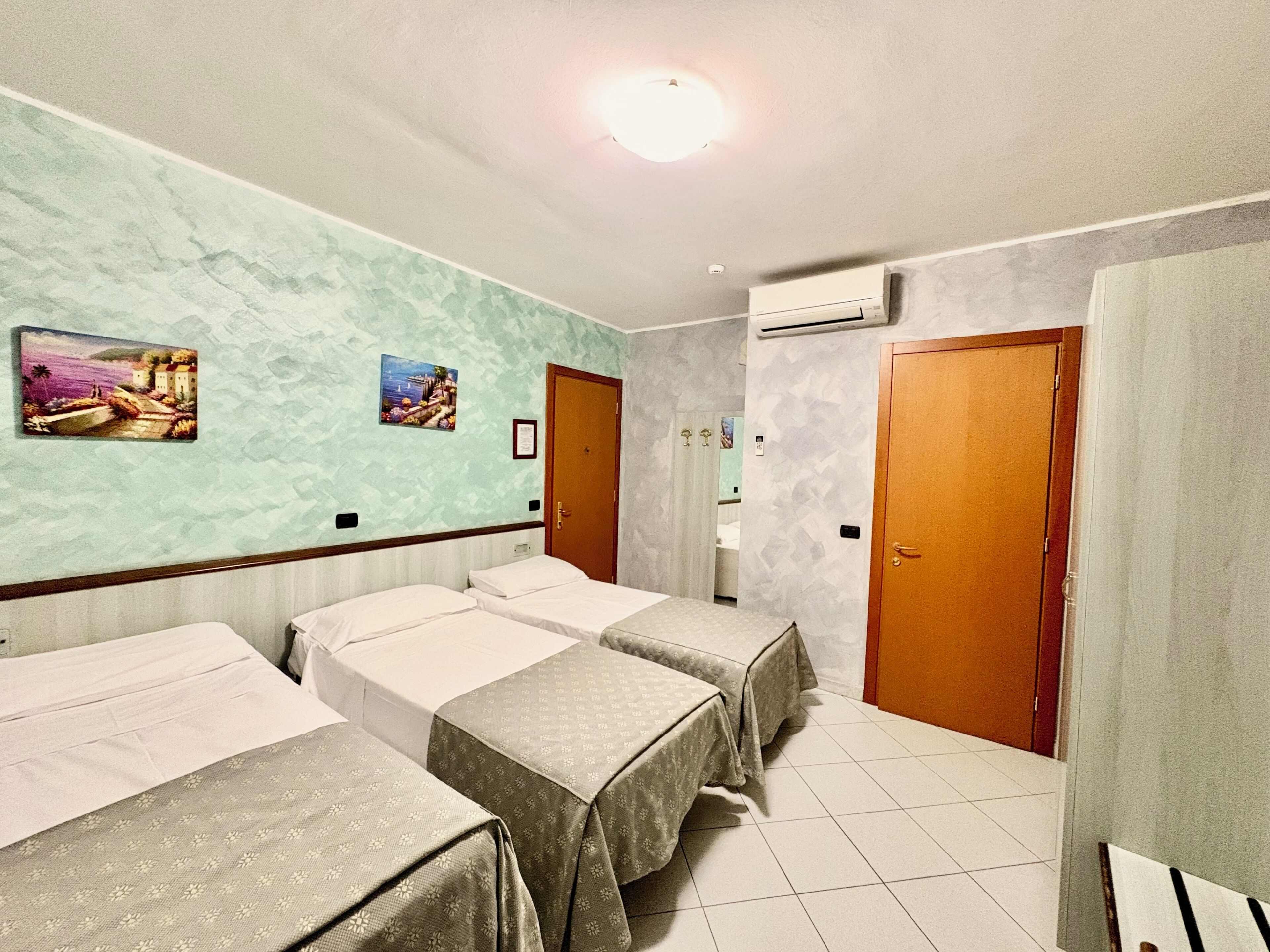 Una habitación de hotel con tres camas, un baño con ducha y dos puertas.