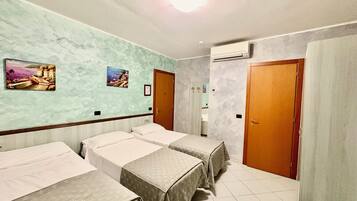 Hotellihuone, jossa on kolme sänkyä, kylpyhuone suihkulla sekä kaksi ovea.