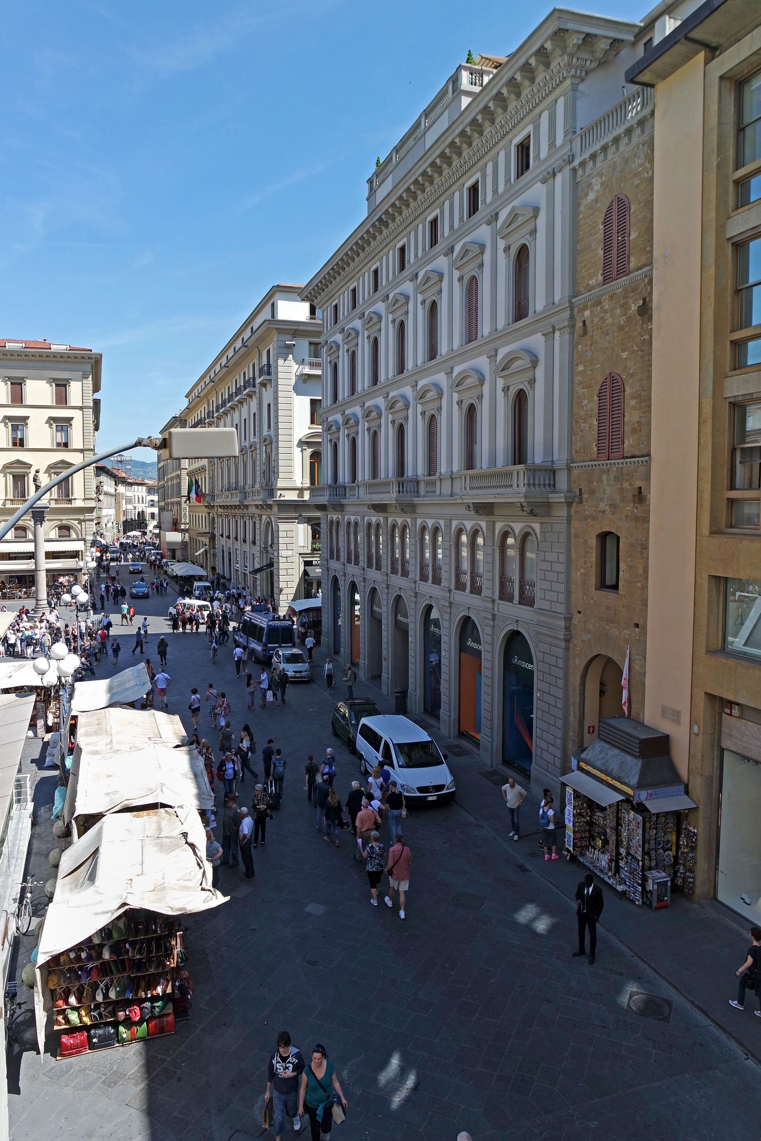 A bustling street with historic buildings, a market stall, and a white van.