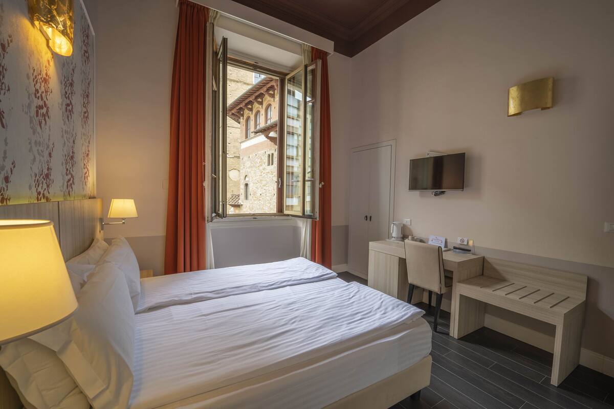 A hotel room with a bed, a desk, a television, and a window with curtains.