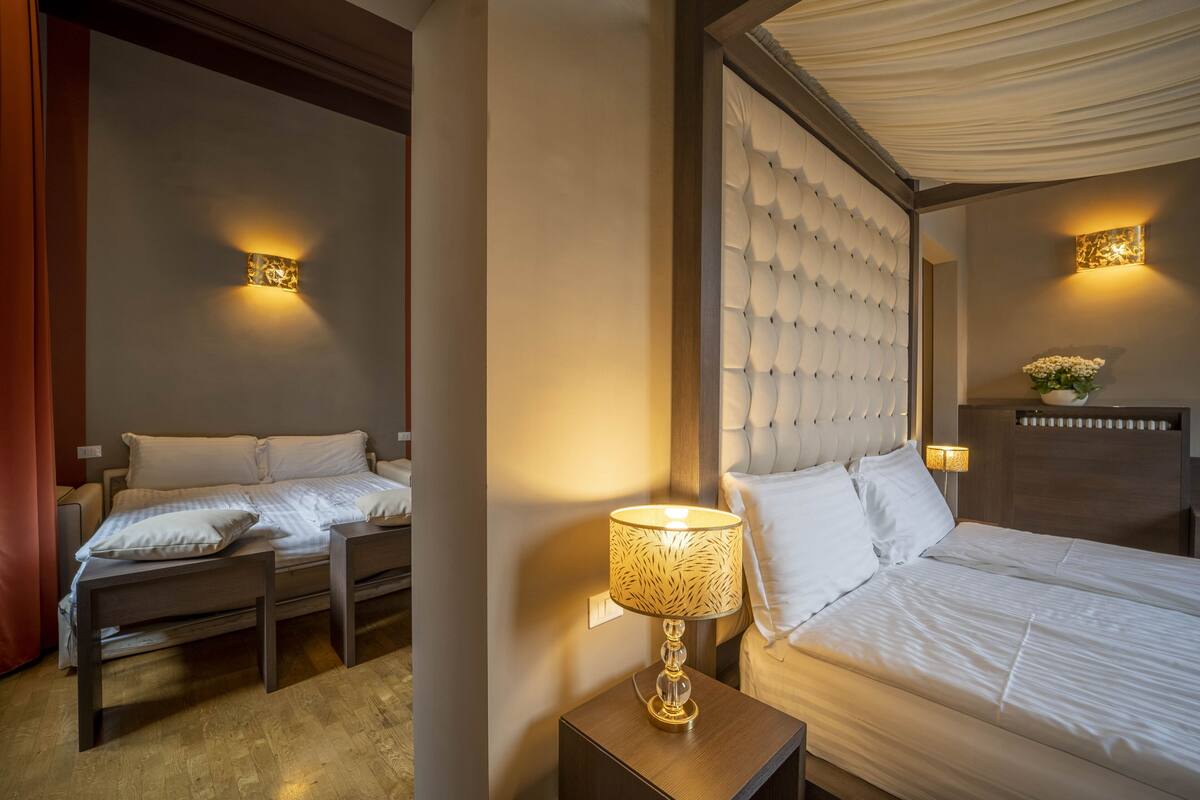 A hotel room with two beds, a nightstand with a lamp, and decorative wall sconces.