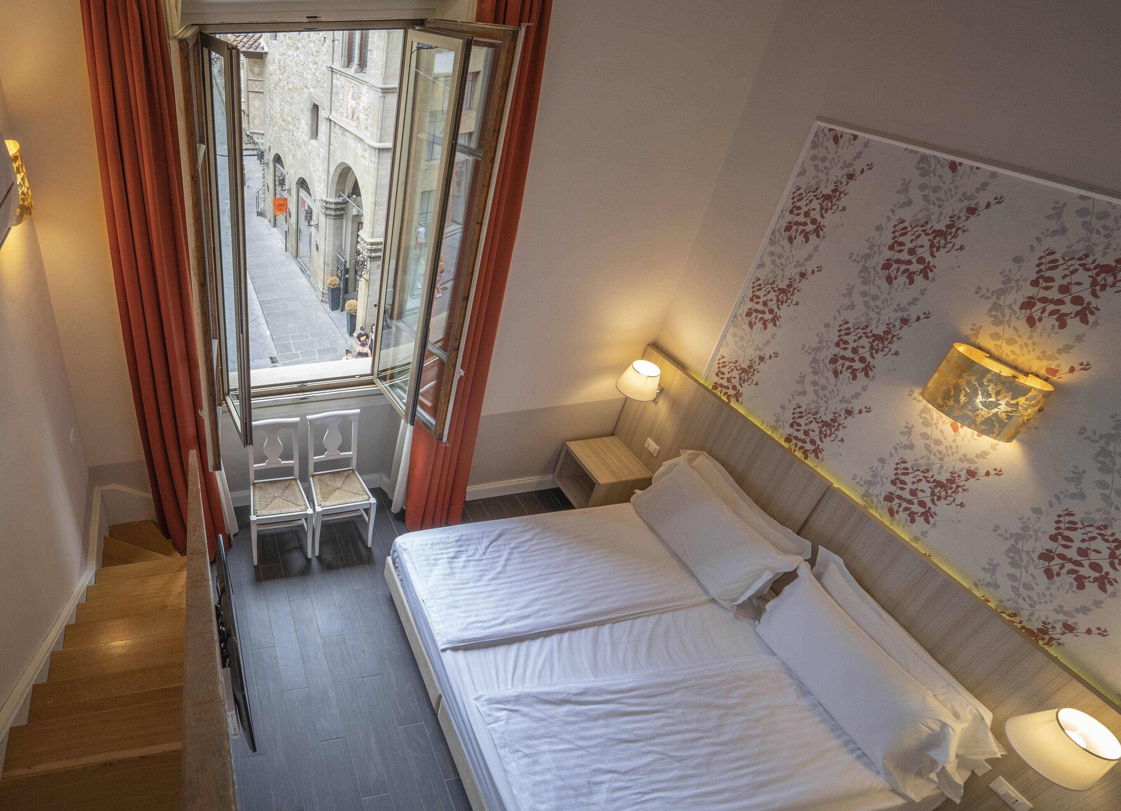 A hotel room with a bed, a nightstand, a lamp, a chair, and a window with curtains.