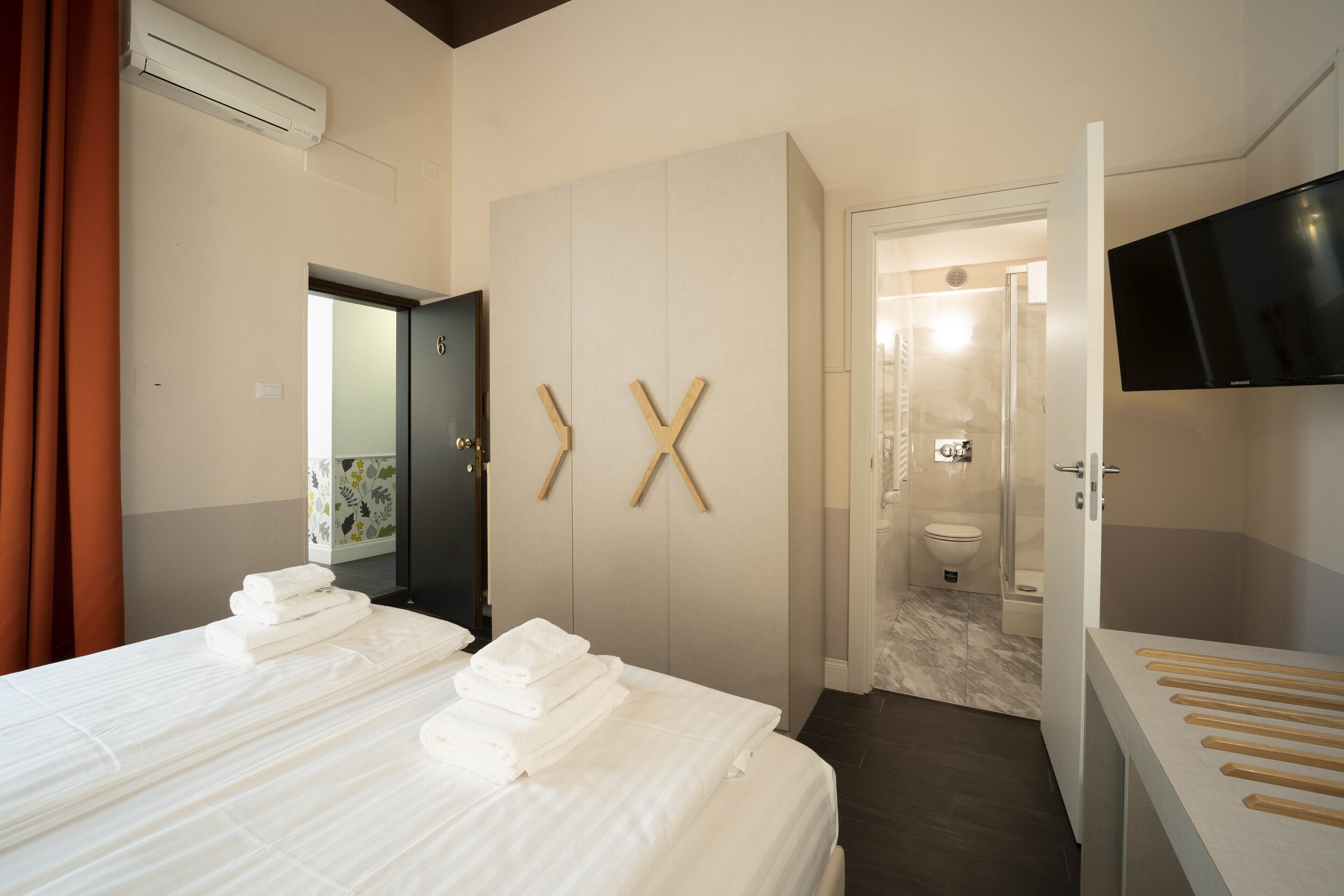 A hotel room with a bed, a wardrobe, a TV, and a bathroom visible through an open door.