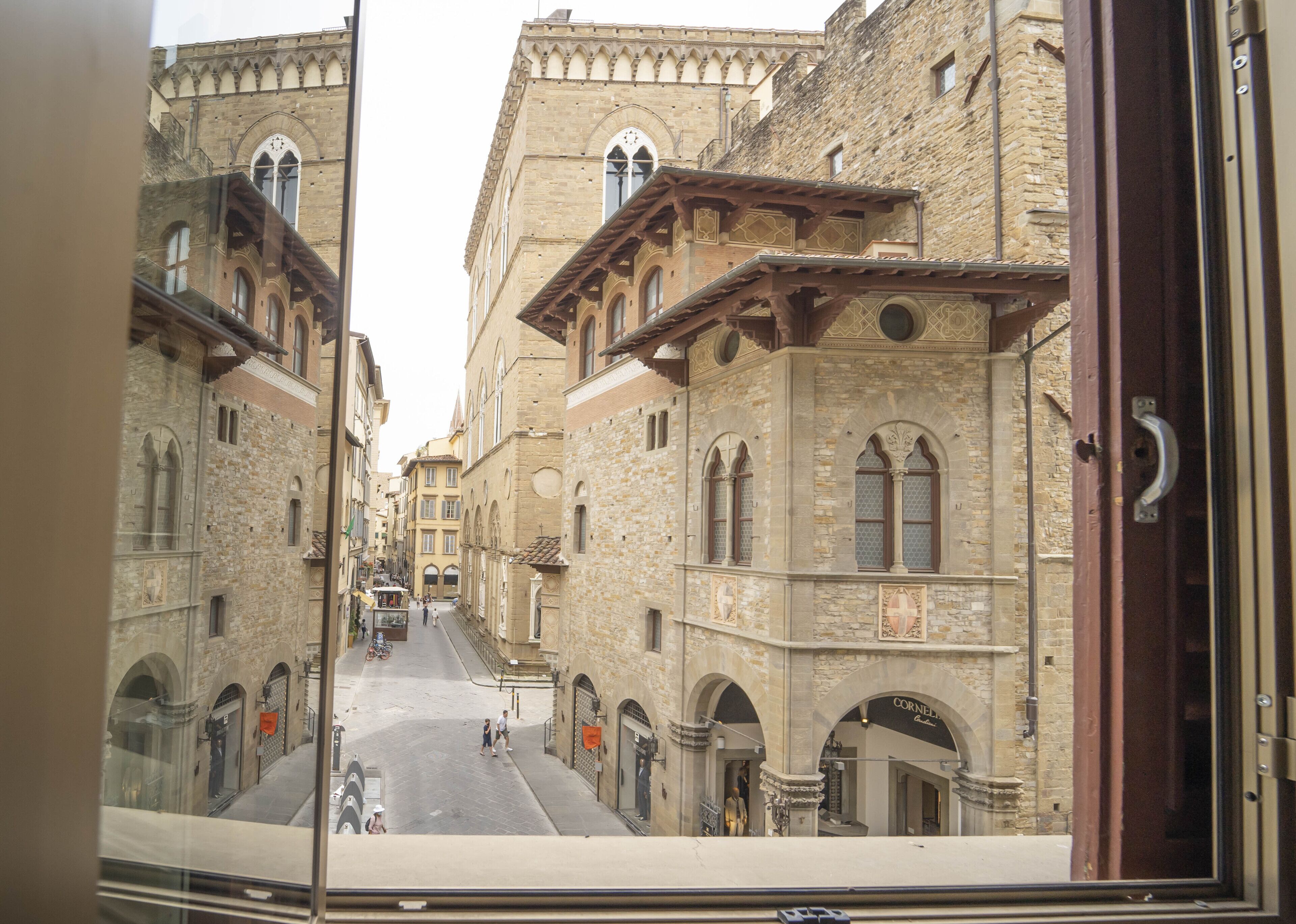 A street view through a window, featuring historic buildings with arched windows and stone facades.