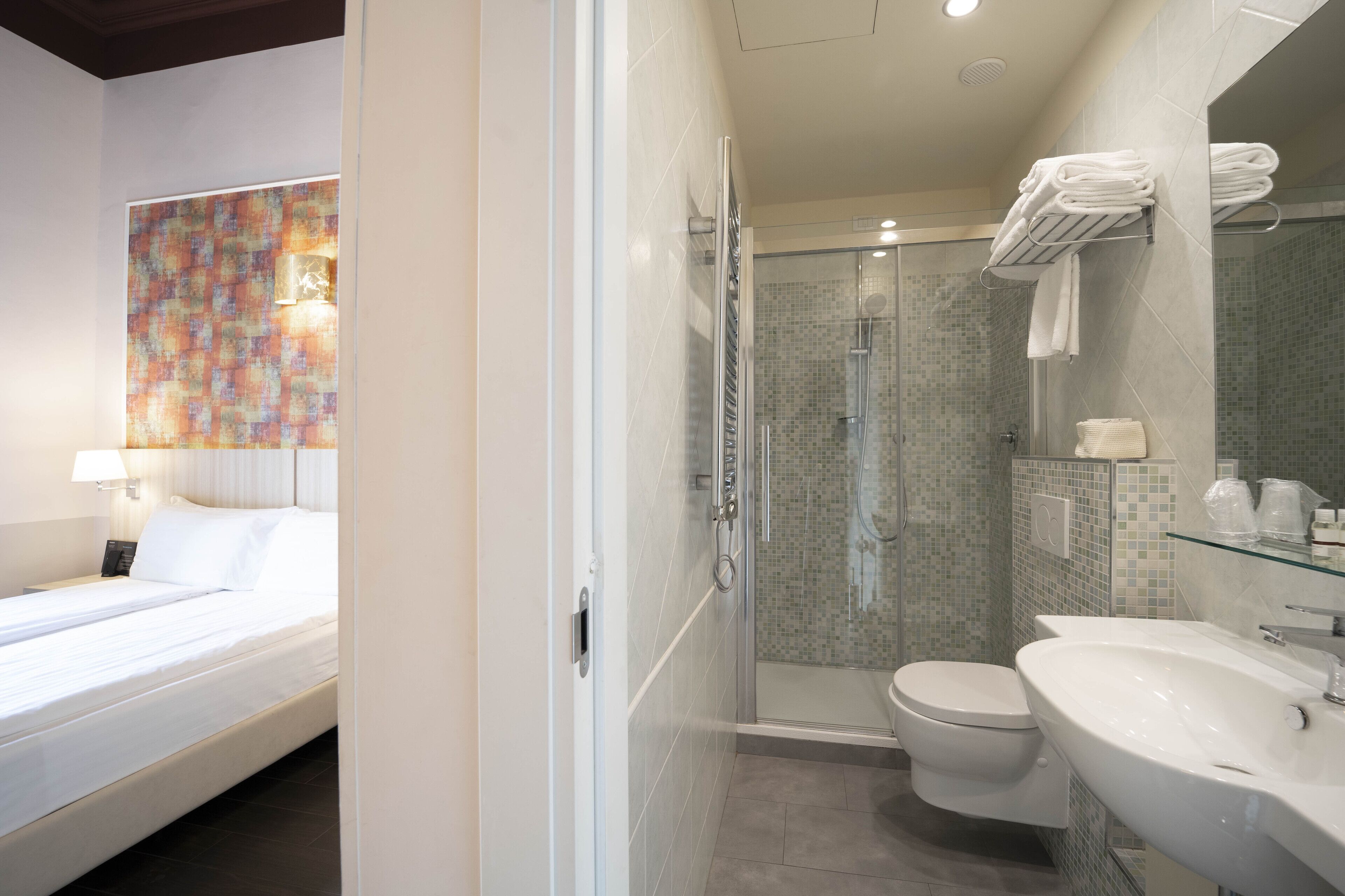 A hotel room with a bed, a shower, a toilet, and a sink.