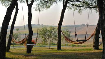 A hammock swing between trees in a grassy field with a distant view of a landscape.