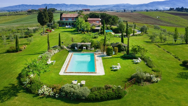 A large, rectangular swimming pool surrounded by a well-maintained lawn, with a house and garden in the background. - Casa Bellavista (Cortona)