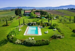 Una gran piscina rectangular rodeada por un césped cuidado, con una casa y jardín al fondo.