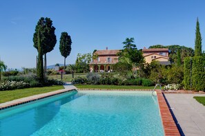 A swimming pool with a brick border, surrounded by well-maintained gardens and tall trees. - Casa Bellavista (Cortona)