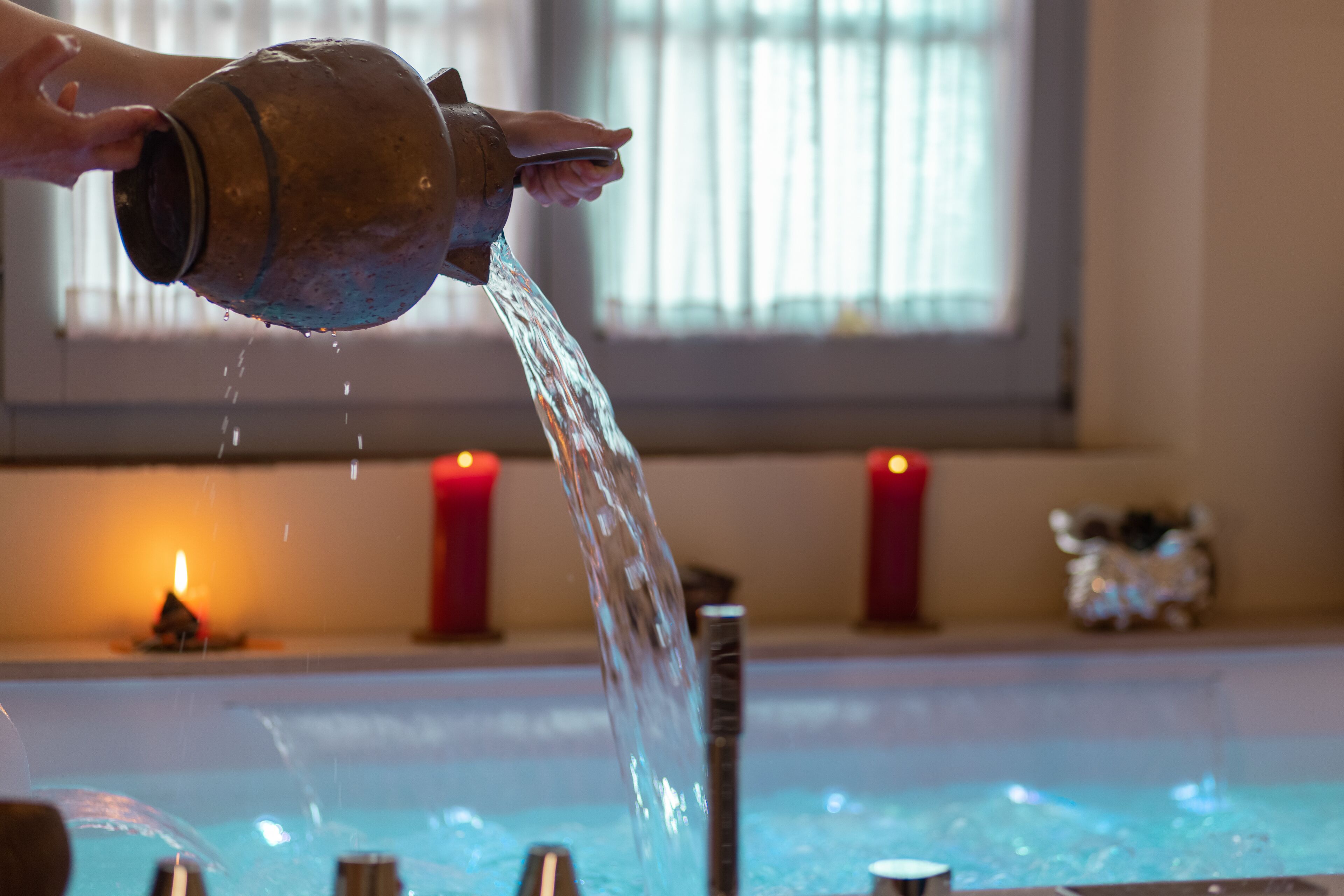 Une main verse de l’eau d’un pichet en métal dans une baignoire.