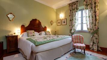 Un dormitorio con cama, una silla, una mesita de noche y una ventana con cortinas florales.