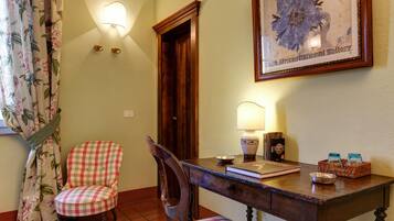 Un rincón comedor con mesa de madera, dos sillas, una lámpara, una obra de arte enmarco y un cortinaje floral.