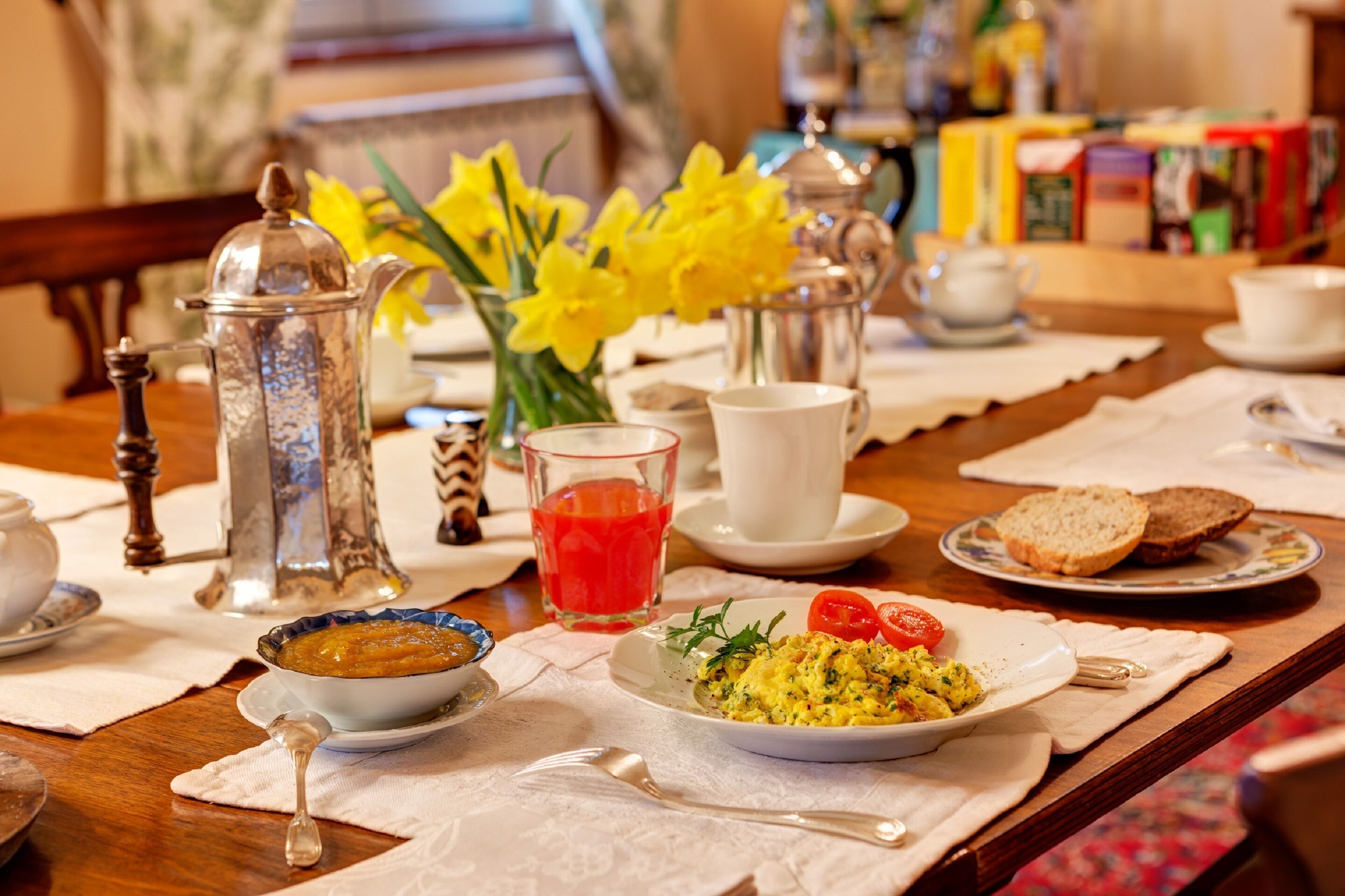 A breakfast setting with a coffee pot, teapot, and a plate of scrambled eggs and tomatoes.