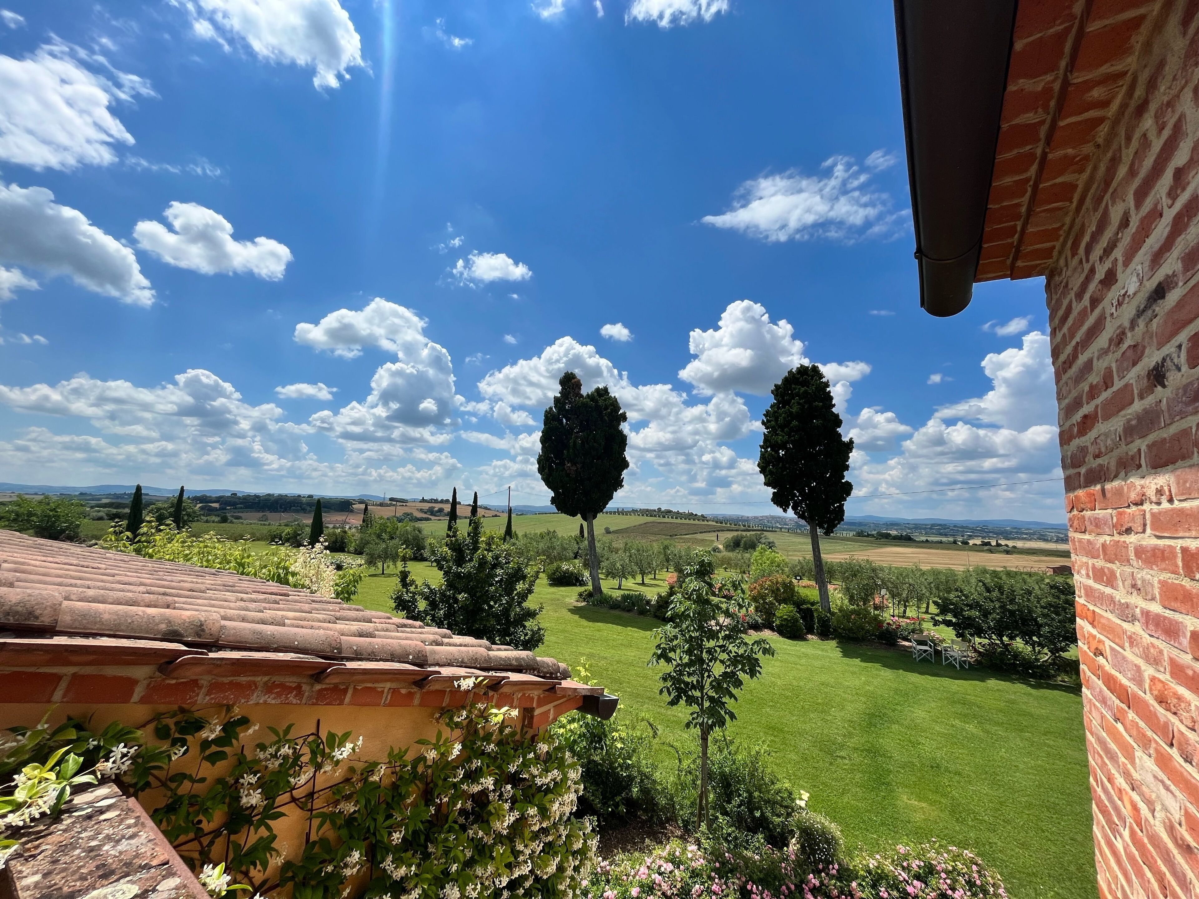 A view from a balcony overlooking a well-maintained garden with a clear blue sky and distant hills.