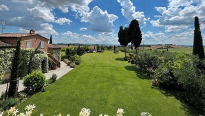A well-maintained lawn with a brick house and a flag, surrounded by trees and a clear sky. - Casa Bellavista (Cortona)
