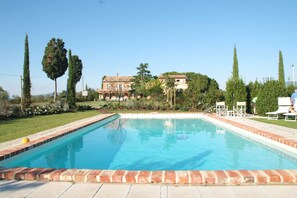 A rectangular swimming pool with a brick border, surrounded by a well-maintained lawn and tall trees. - Casa Bellavista (Cortona)