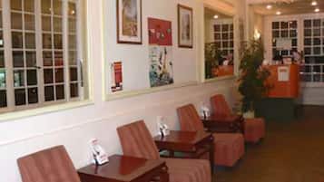A hotel lobby with a reception desk, several wooden chairs, and framed artwork on the walls.