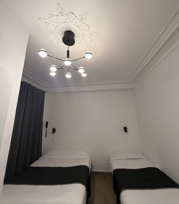 A room with two beds, a ceiling light fixture, and a wall-mounted telephone. - Hôtel Du Brabant (Paris)