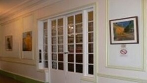 A hallway with white walls, green trim, and a red doormat. There are framed pictures on the wall and a door with glass panels.