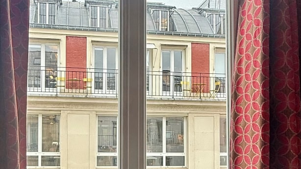 A balcony with a potted plant, a metal railing, and a view of a multi-story building with balconies.