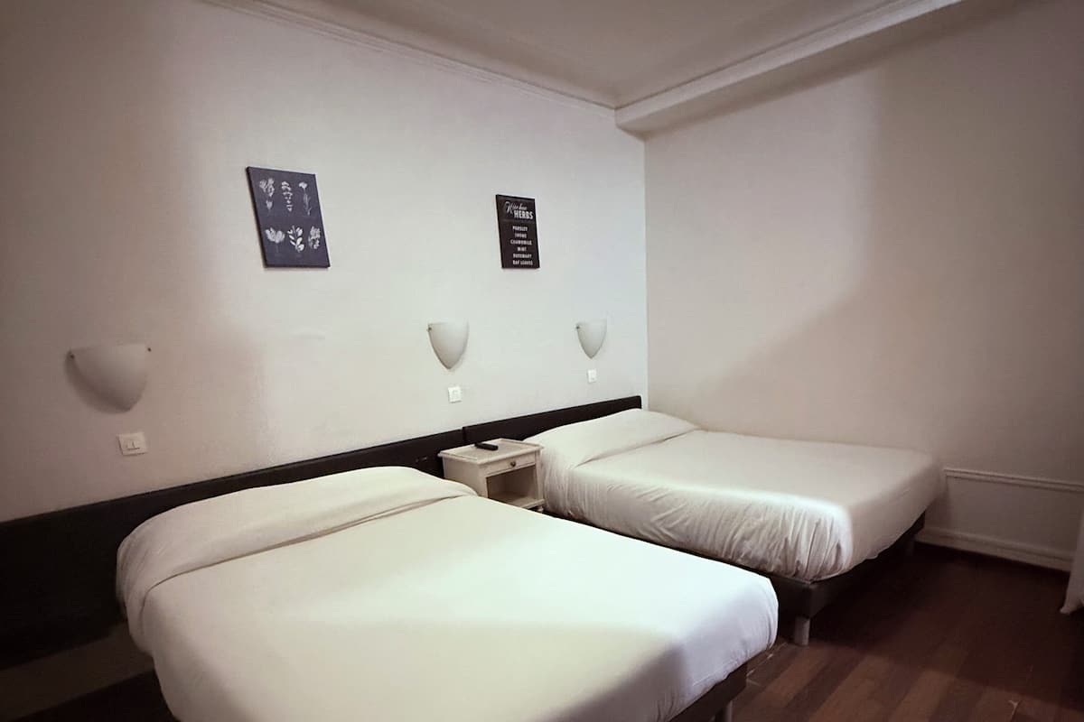 A hotel room with two single beds, a nightstand, and wall-mounted light fixtures.