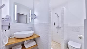 A modern bathroom with a white sink, mirror, and shower. There are towels and a scale on the counter.